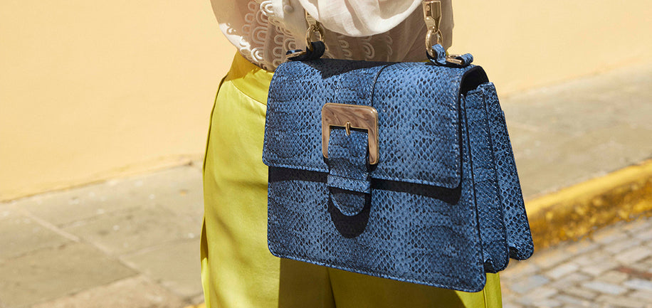 Navy Bonaire Small Hallie with a buckle detail held by a person wearing yellow pants.