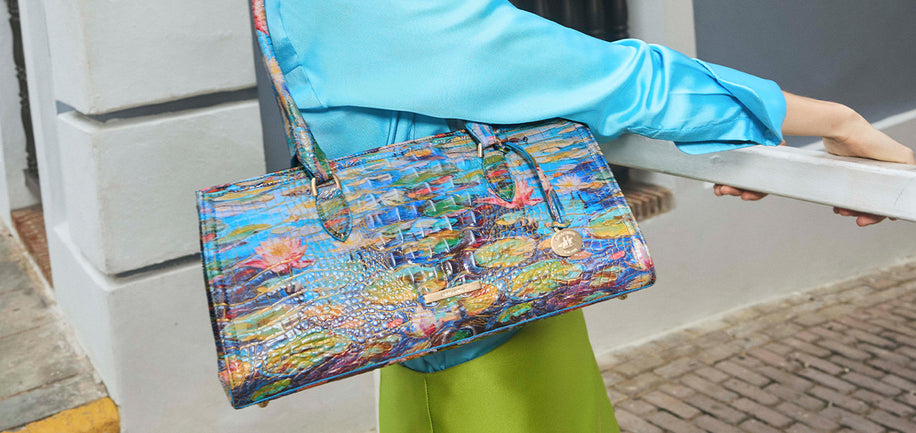 Person holding Waterlily Melbourne Sophia satchel, wearing a blue top and green pants.