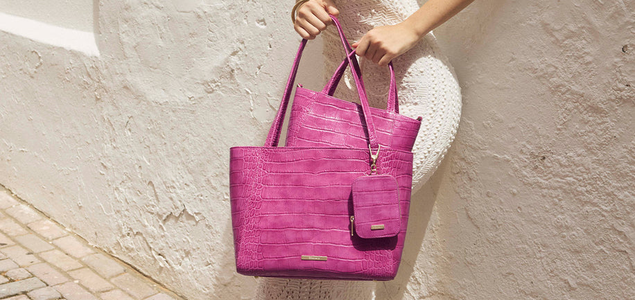 Person holding a pink tote bag against a light stone wall.