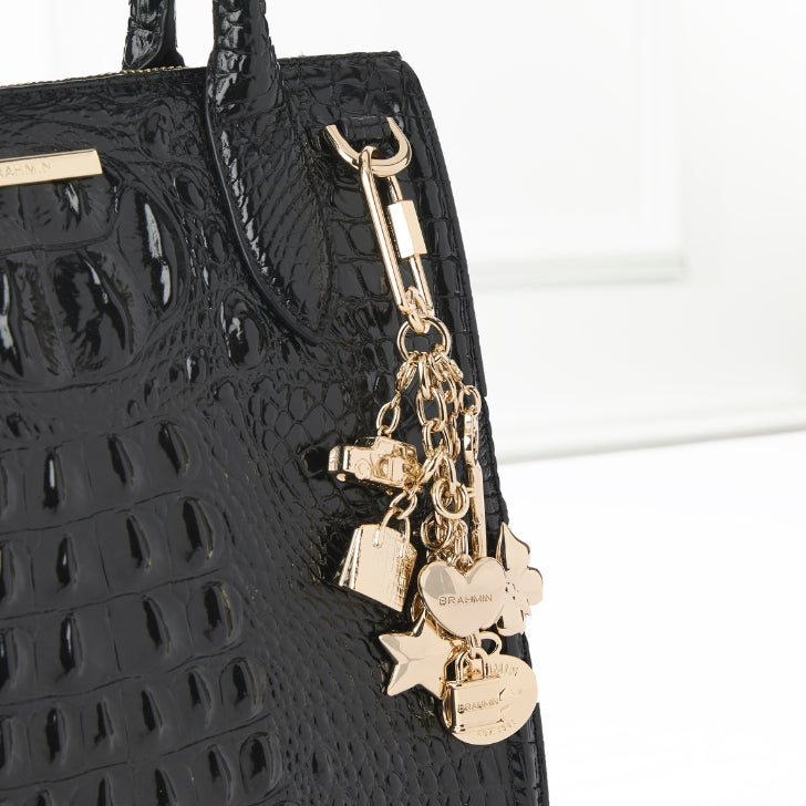 Close-up of a black embossed Brahmin handbag adorned with a gold charm keychain featuring heart, star, and lock shapes.
