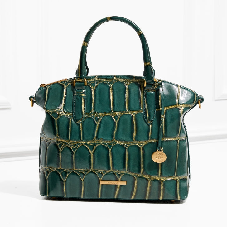 Brahmin deep green croc-embossed satchel with gold-tinted texture, structured silhouette, double top handles, and signature gold medallion charm, photographed in a white studio setting.