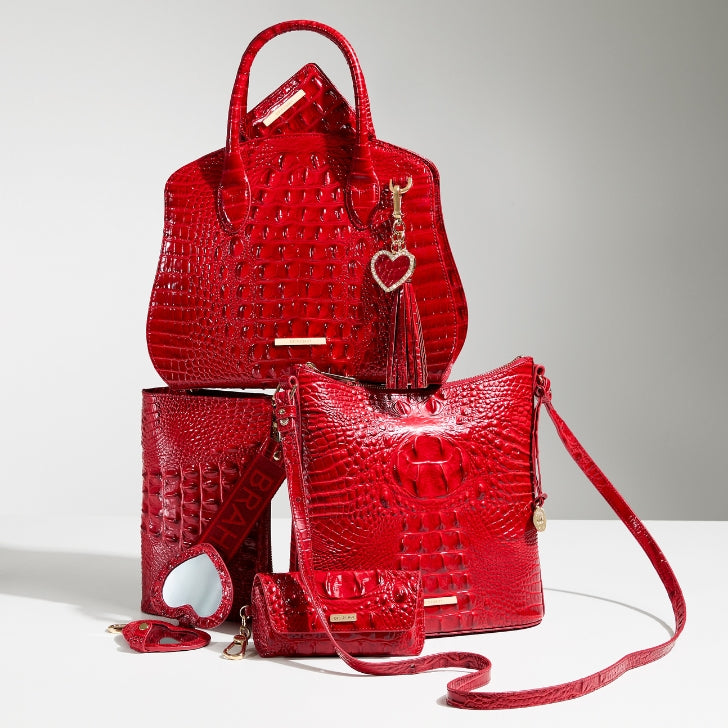 Red croc-embossed leather handbag collection featuring a structured satchel, zip-top crossbody bag, wristlet, compact wallet, coin pouch, and coordinating heart charm accessories, styled together on a white background
