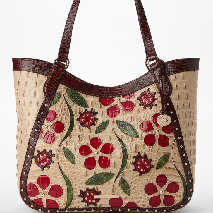 Brahmin Ladybird Aliza tote in cream croc-embossed leather with red floral and ladybug appliqués, green leaf accents, dark brown trim and gold-tone studs, on white background.