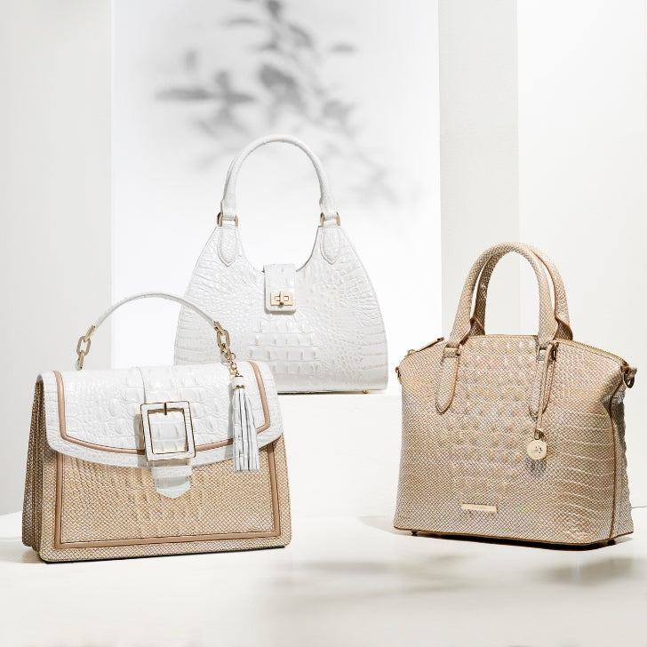 Sophisticated Brahmin handbag trio including a white satchel with gold clasp, a structured beige-and-white satchel with buckle and tassel, and a metallic gold dome satchel, all with signature crocodile embossing.