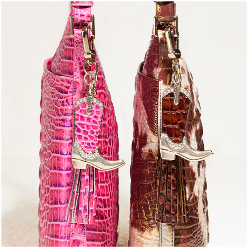 Side view of two Brahmin croc-embossed leather bags in bright pink and brown cowhide, each with tassel and gold boot-shaped charm dangling