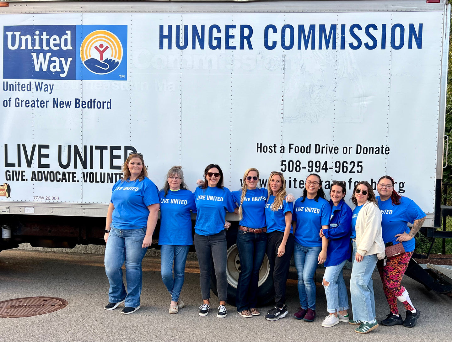 Group of volunteers in blue ‘Live United’ shirts standing in front of a United Way Hunger Commission truck, smiling together during a community event.