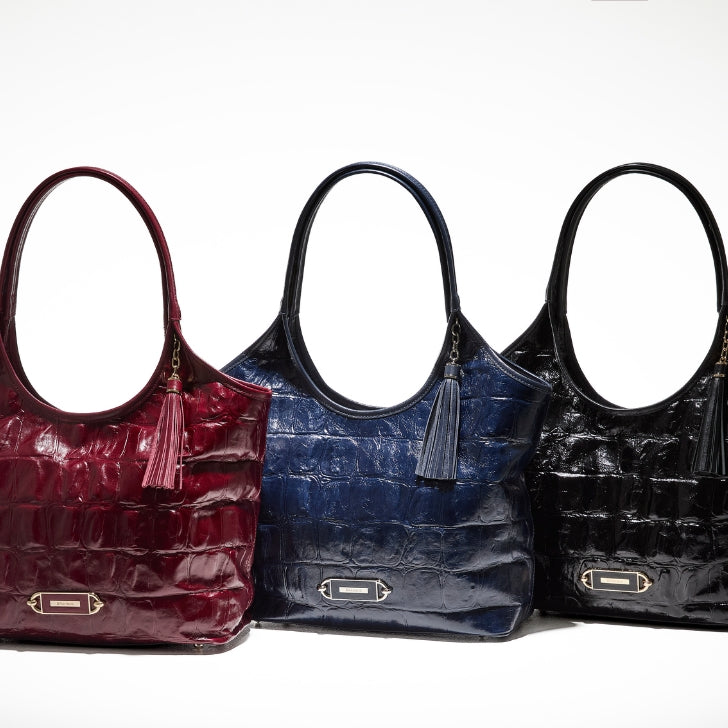 Women’s croc-embossed leather work totes with tassels in red, blue, and black.