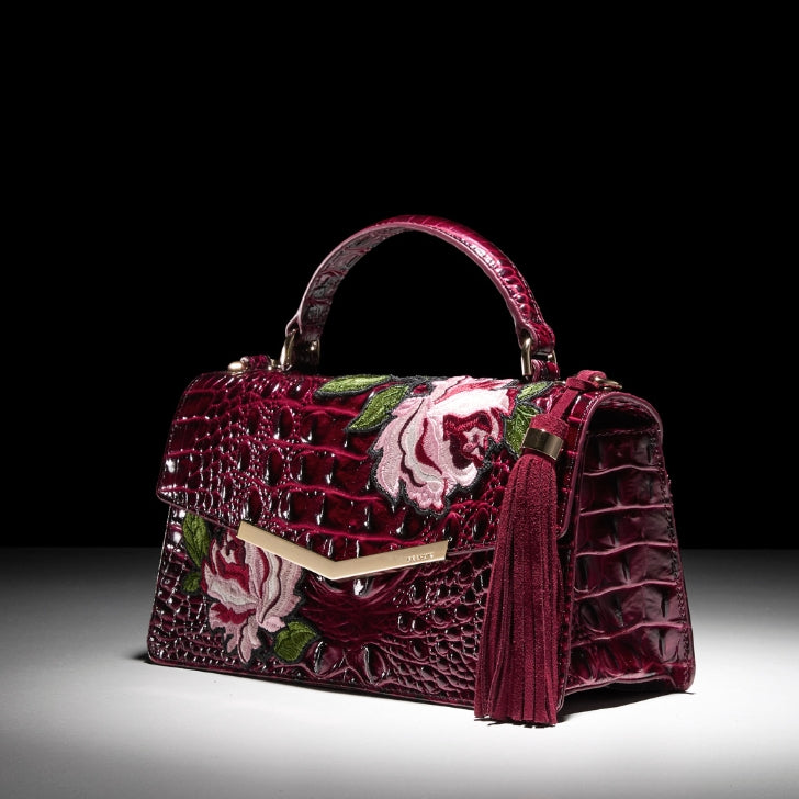 Brahmin deep burgundy embossed leather satchel with embroidered pink floral design, gold hardware, and tassel detail.