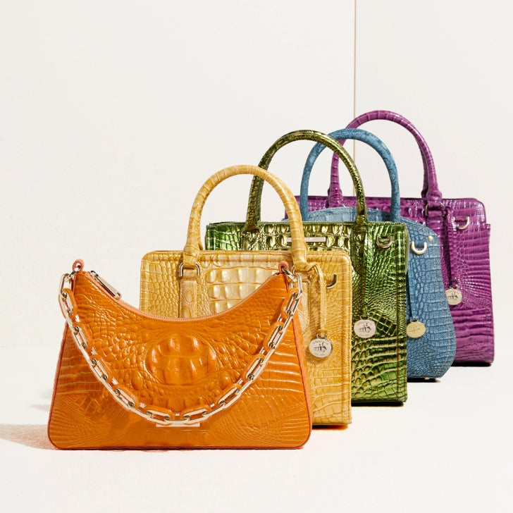 Colorful lineup of Brahmin croc-embossed handbags in orange, yellow, green, blue, and purple with silver and gold hardware.