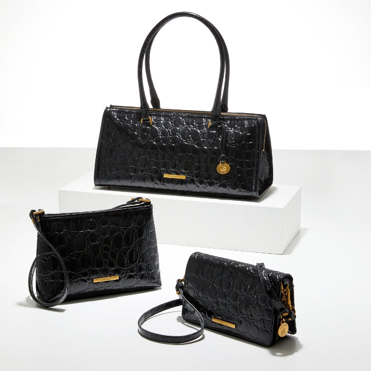 Black crocodile‑embossed Brahmin Sophia tote on a white pedestal, flanked by a matching Lorelei wristlet on the left and a Minuette crossbody bag on the right.